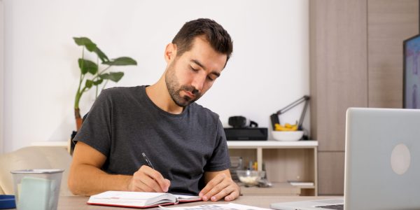 Man writing on notebook at his desk. Putting thoughts on paper.